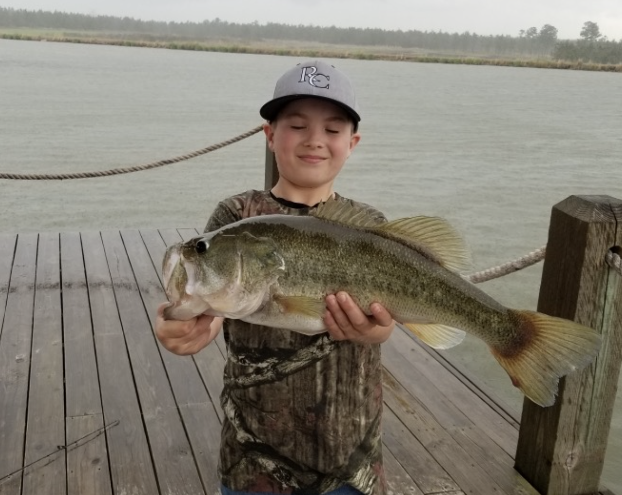 boy holding a very big largemouth bass by a lake